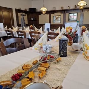 Clubraum mit eingedeckten Tischen, herbstlicher Tischdekoration, Holzstühlen und Deckenleuchten