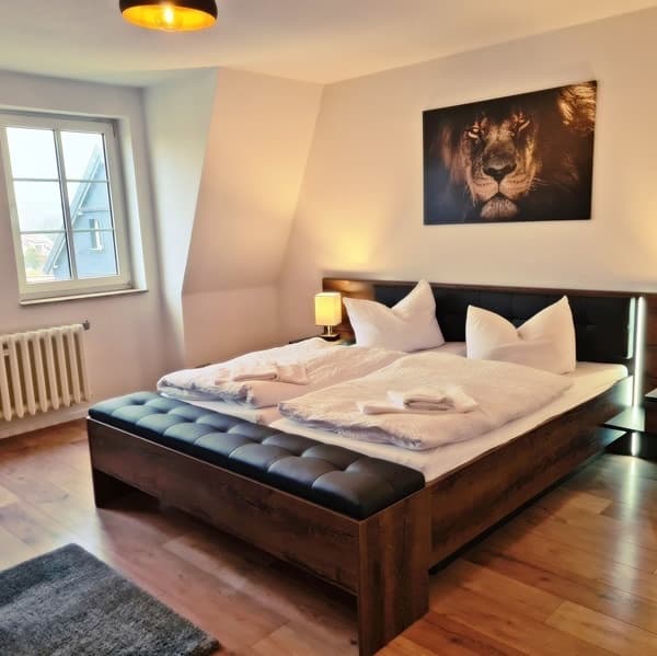 Heller Raum unter der Dachschräge mit Doppelbett, lederner Bettbank, Dielenboden und einem großformatigen Löwenbild über dem Kopfteil