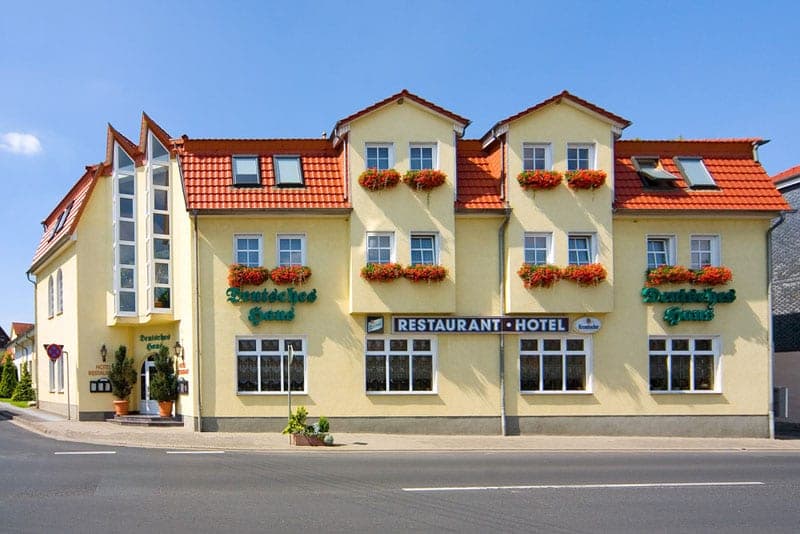 Straßenfront des Hotels Deutsches Haus mit roten Blumenkästen an allen Fenstern und dem Schriftzug „Restaurant · Hotel“