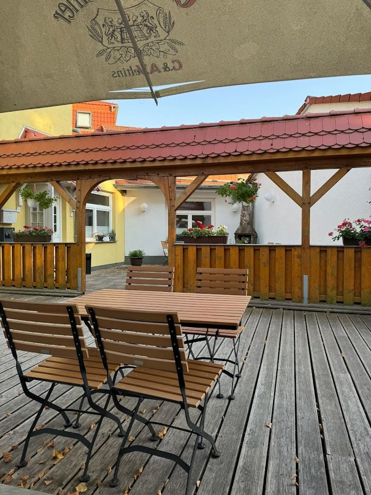 Biergarten des Hotels Deutsches Haus: Holztische und Klappstühle auf einer Holzterrasse, daneben ein überdachter Gang mit Blumenkästen